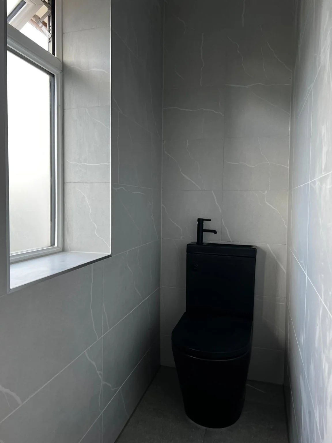 Finished black toilet with grey tiled walls and window